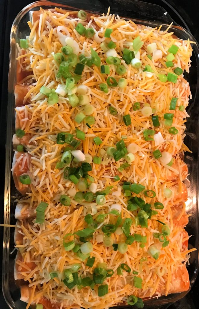 Sprinkle cheese and diced green onions on top of beef enchiladas.